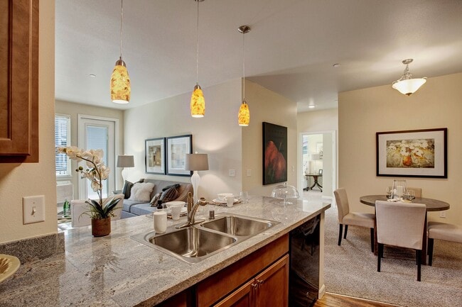 A kitchen with our sleek appliances and stone countertops with a view into the dining area and living room - Solara Apartments