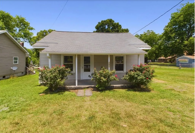 Front Exterior: A cozy covered porch surrounded by vibrant landscaping with blooming rose bushes. - 1011 Elm St Casa