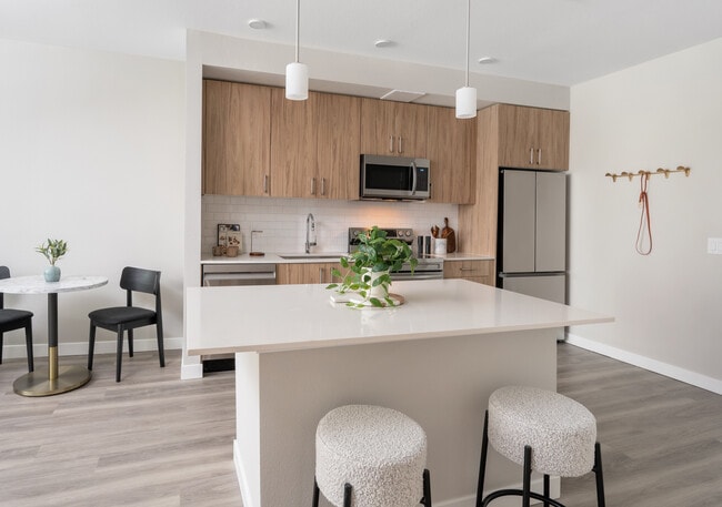 Finish Package II Kitchen with oak cabinetry, white quartz countertops, white tile backsplash, stainless steel appliances, pendant lighting, and hard-surface vinyl plank flooring