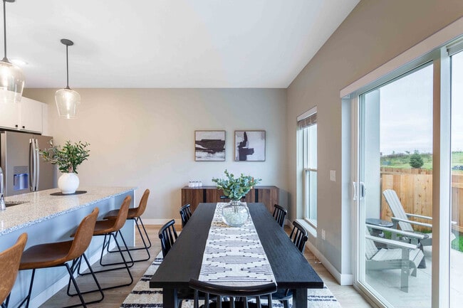 Contemporary dining area with elegant decor, featuring a granite kitchen island, stylish pendant lights, and a view of the lush outdoor patio. - Summerwell Maple Grove