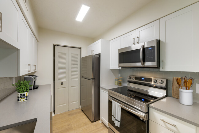 Renovated Meadows II kitchen with stainless steel appliances, white cabinetry, grey quartz countertops, grey tile backsplash, and hard surface flooring - Avalon Fairway Hills-Meadows Apartments