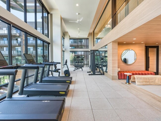 Light-filled fitness center with premium cardio and strength equipment plus relaxing lounge seating nearby.