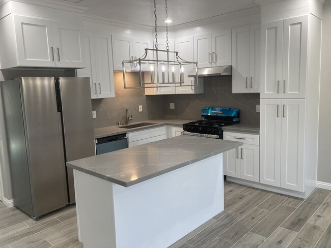 Spacious kitchen with island, quartz countertops, white shaker cabinets and stainless steel applianc - 10508 Mattock Ave Condo Unit A