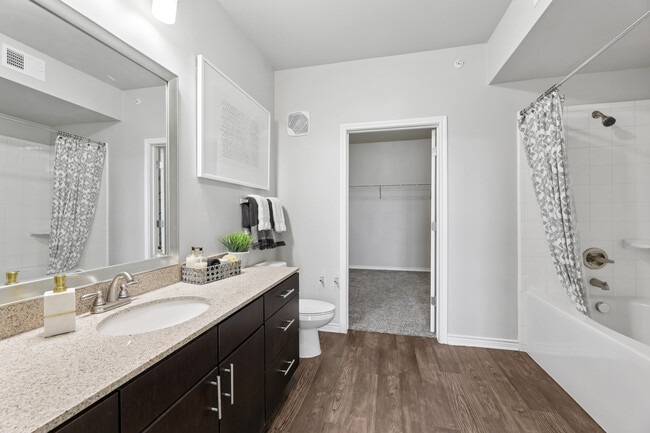 Bath with dark cabinetry, beige speckled granite countertops, and hard surface flooring