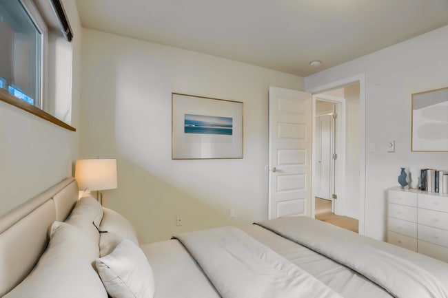 A bright and inviting bedroom featuring a comfortable bed, natural lighting from the window, and a door leading to an adjacent room. - Alaska 45