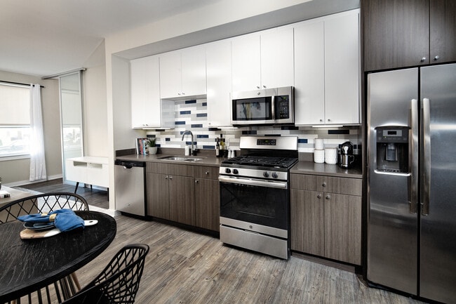 Modern Package kitchen with white and dark brown cabinetry, dark grey granite countertops, multi-colored subway tile backsplash, stainless steel appliances, and hard surface flooring