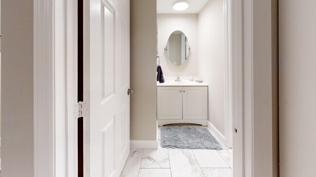 Bright and modern bathroom with chic tile flooring, elegant vanity, and a stylish oval mirror. - Chateau of Tampa