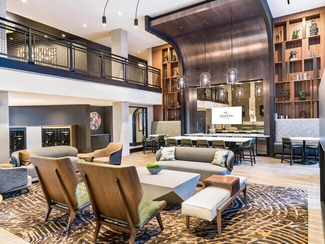Double-height community lounge with layered seating, a shared kitchen, and warm wood details designed for conversation, hosting, and everyday gathering.