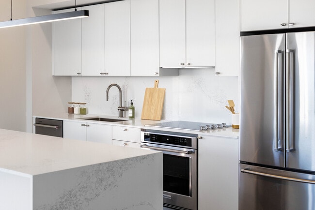 Signature Collection kitchen with white cabinetry, white marbled quartz countertop and backsplash, wine fridge, and upgraded stainless steel appliances - Avalon South Miami