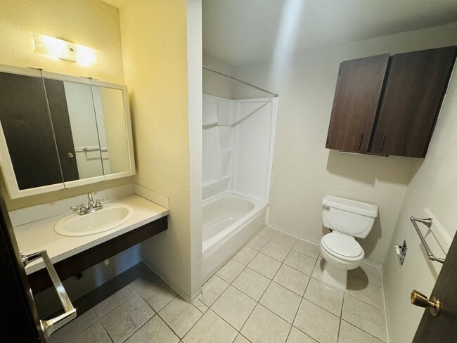 This spacious bathroom features a full tub and shower, ample storage, and easy-care tile flooring for everyday comfort.