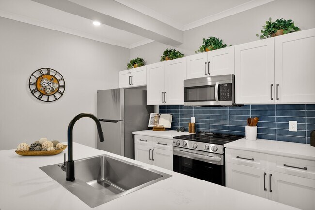 Modern kitchen with sleek stainless steel appliances, elegant white cabinetry, and a stylish island for casual dining. - Pointe Grand Statesboro