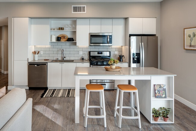 Open concept kitchen with quartz countertops, island, tile backsplash, and stainless steel appliances - AVA Hollywood at La Pietra Place Apartments