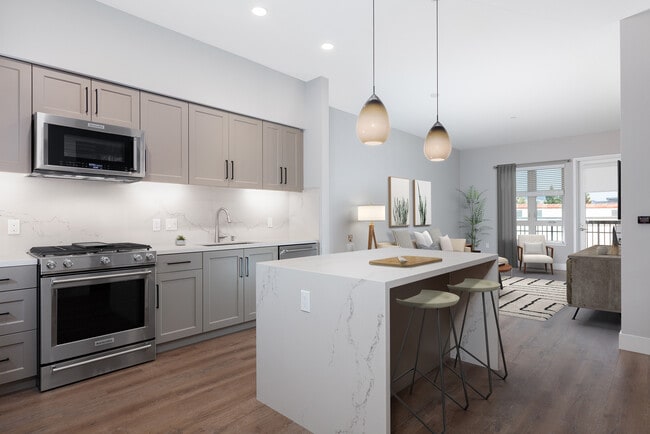 Signature Collection kitchen with upgraded stainless steel appliances, grey cabinetry, white marble countertops and backsplash, and hard surface flooring - Avalon Walnut Creek Apartments