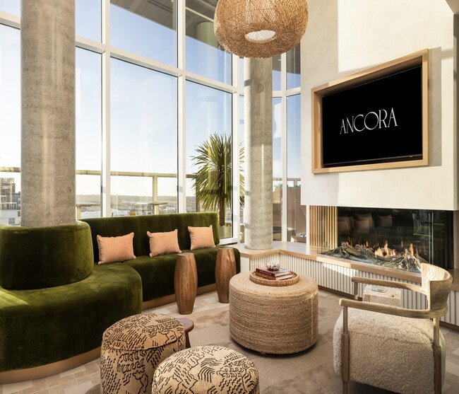 Luxurious apartment living room featuring a modern green velvet sofa, large windows with stunning views, a cozy fireplace, and elegant decor.