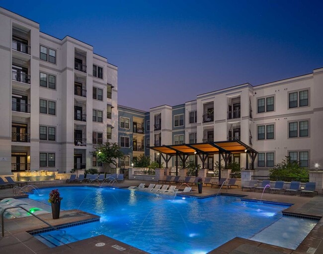 Dusk shot of pool with in-water lounge seats, additional lounge chairs, lighted fountain and covered area - Elle of Buckhead Apartments