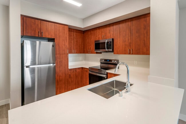 Renovated Package I kitchen with stainless steel appliances, white quartz countertops, cherry cabinetry, and hard surface flooring