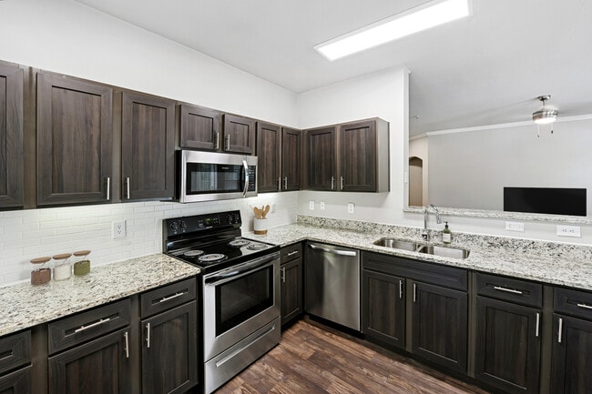 Classic Package II kitchen with stainless steel appliances, espresso cabinetry, white subway tile backsplash, speckled granite countertops, and hard surface flooring