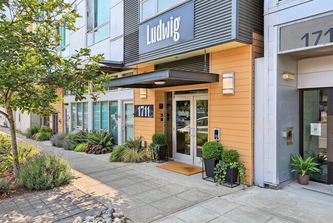 Secure main entrance at Ludwig Apartments in Seattle, featuring contemporary exterior finishes and landscaped sidewalk entry.