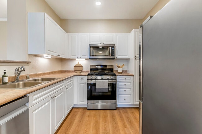 Renovated Package I kitchen with upgraded stainless steel appliances, white cabinetry, neutral laminate countertops, and upgraded hard surface flooring