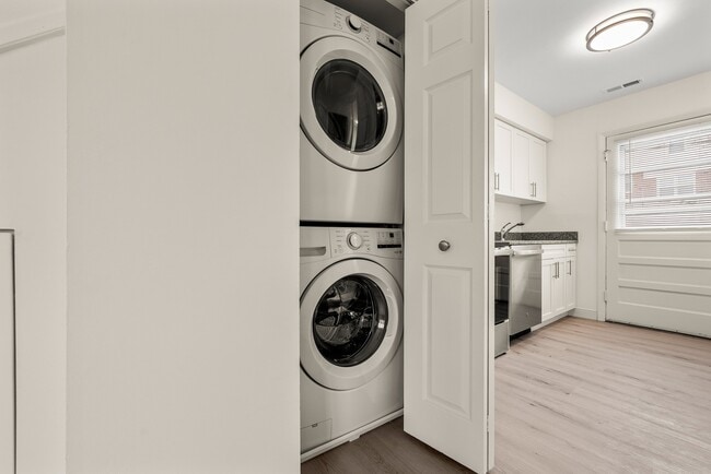 Modern apartment interior with a sleek stackable washer and dryer set in a closet next to a bright kitchen featuring white cabinets - Stony Brook Commons