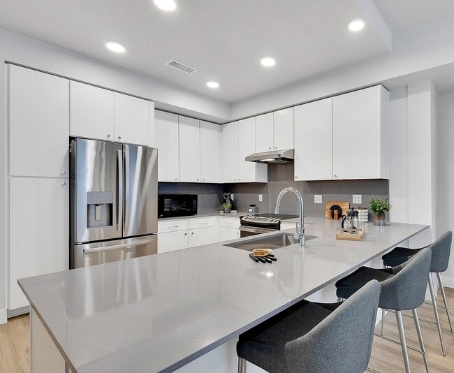 Modern kitchen with sleek white cabinets, stainless steel appliances, elegant countertops, and cozy bar seating. - The Dorsey