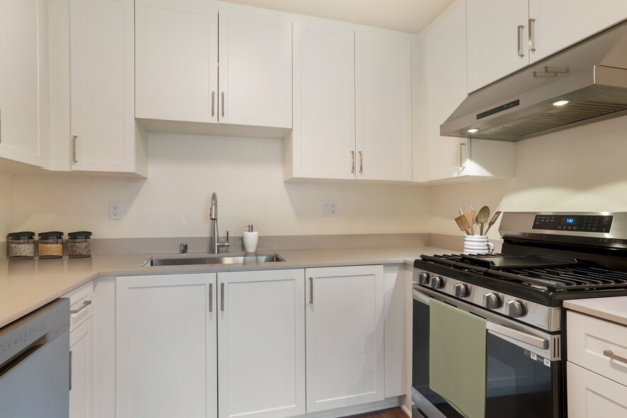 Renovated Package I kitchen with stainless steel appliances, white cabinetry, beige granite countertops, and hard surface flooring