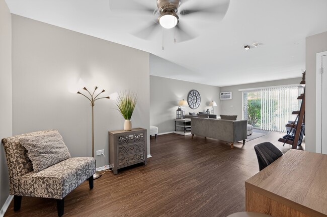 Relax in a bright living room featuring a cozy chair and fresh greenery at Renaissance at Carol Stream in Carol Stream, IL. - Renaissance at Carol Stream
