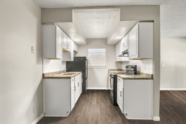 Charming kitchen with sleek black appliances, elegant white cabinets, and inviting wood flooring. - Alderman Park Apartments