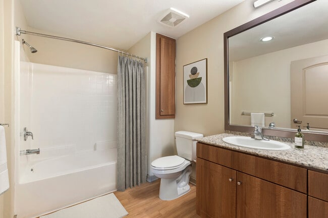 Renovated Package I bath with oak cabinetry, beige speckled granite countertops, and hard surface flooring