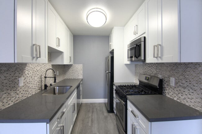 Cocina con encimeras de piedra de cuarzo y electrodomésticos de acero inoxidable, horno de microondas, horno, refrigerador, y accesorios.