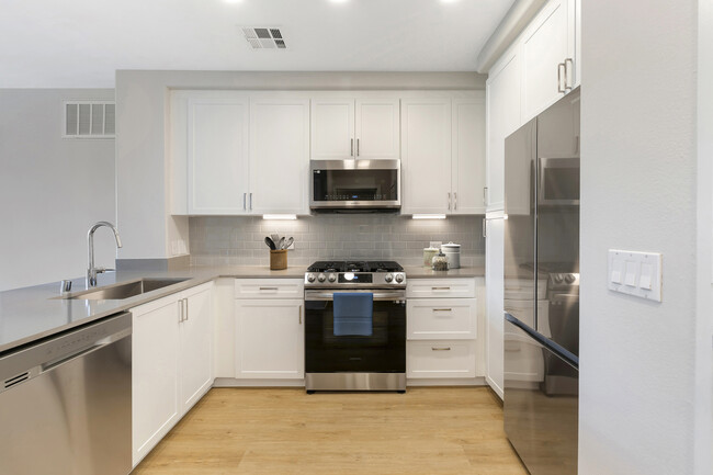 Renovated Package I kitchen with stainless steel appliances, grey quartz countertops, white cabinetry, grey tile backsplash, and hard surface flooring - Avalon Encino Apartments