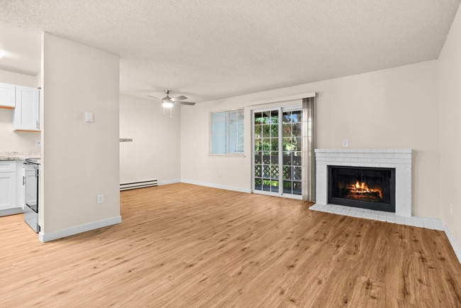 Bright and inviting living space featuring a cozy fireplace, elegant wood flooring, and large sliding glass doors with garden views. - Crossroads at Meridian Apartments