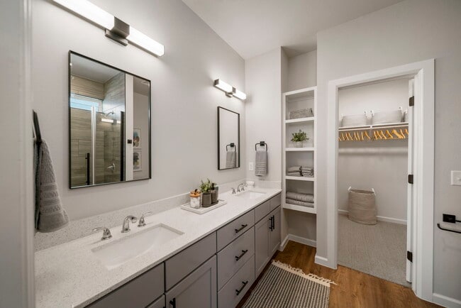 Double vanity bathroom with quartz countertops, framed mirrors, built in shelving, and walk in closet