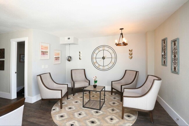 Community seating area with upholstered chairs, round rug, coffee table, wall decor, and modern chandelier lighting