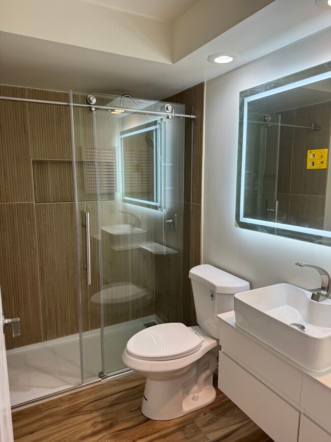 Modern bathroom with glass shower, floating vanity, vessel sink, and LED-lit mirror. - 328 N Allen St Unit 1