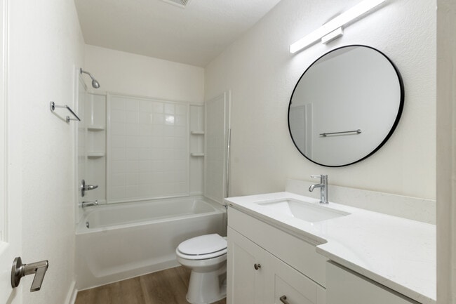 Modern bathroom featuring sleek white cabinetry, elegant round mirror, and pristine bathtub with contemporary fixtures.