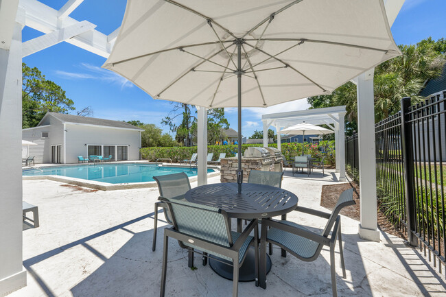 Acogedora zona de piscina al aire libre con cómodos asientos bajo sombrillas, una moderna barbacoa y exuberante vegetación, perfecta para relajarse y recibir invitados. - Vista North
