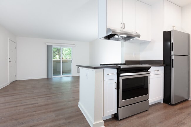 Living area with balcony access and kitchen with white cabinetry, dark grey countertops, stainless steel appliances and hard surface flooring
