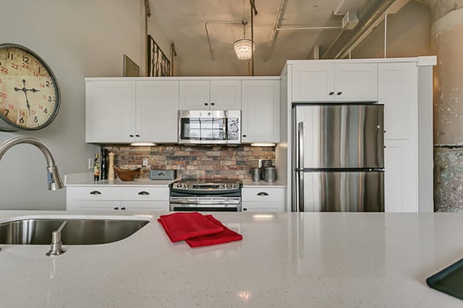 Modern kitchen with white cabinets and brick style backsplash, with white quartz countertop - Lofts at Mockingbird Station Apartments