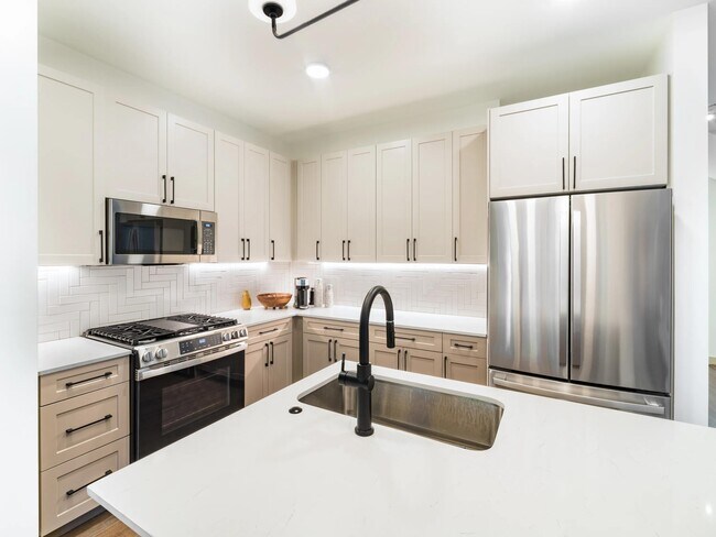 Kitchen with neutral-tone cabinetry, quartz countertops, stainless steel appliances, and a central island designed for gathering, cooking, and everyday living. - Modera Weston