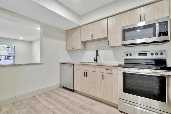 Modern kitchen with sleek stainless steel appliances, elegant wooden cabinetry, and a spacious open layout for comfortable living. - Temple Crest Townhomes