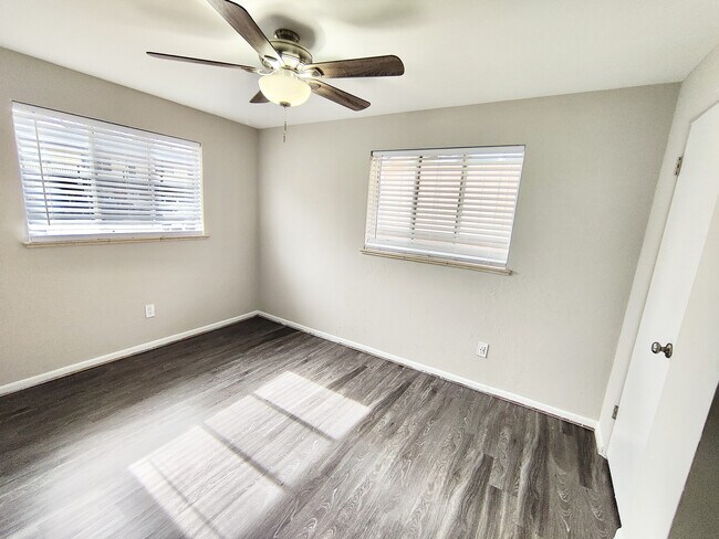 Habitación amplia y luminosa con elegantes pisos de madera oscura y un moderno ventilador de techo, perfecta para un dormitorio acogedor.