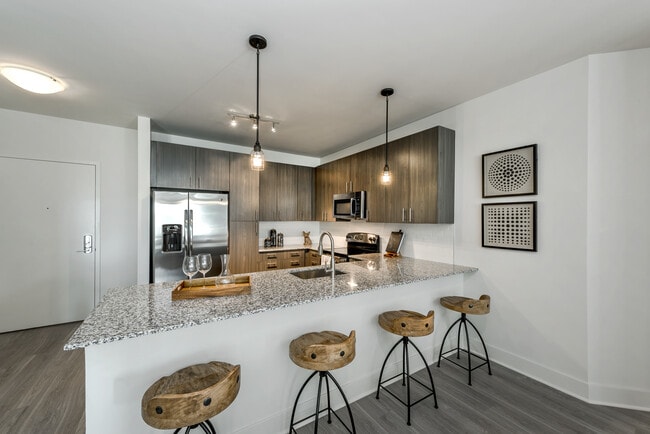 Open concept kitchen with brown cabinetry, granite countertops, stainless steel appliances, tile backsplash and hard surface flooring