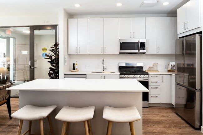 Showroom kitchen with stainless steel appliances, white quartz countertop, light grey cabinetry, and hard surface flooring