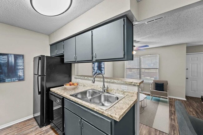Kitchen with gray cabinets, granite countertops, double stainless sink, black refrigerator, and open view to living area