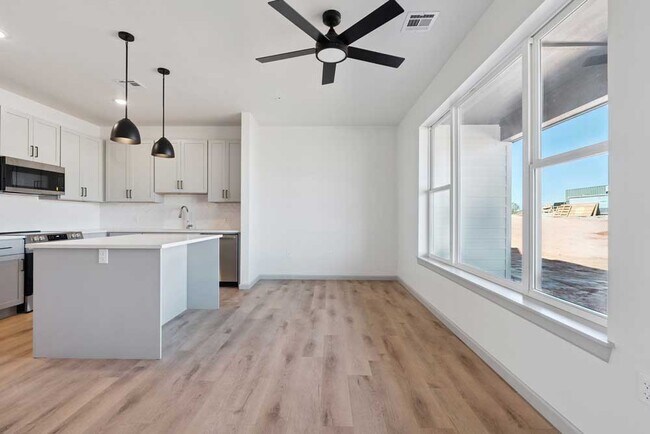 Bright kitchen and dining space with oversized windows, white cabinetry, ceiling fan, and spacious island