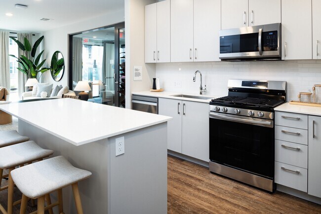 Showroom kitchen with stainless steel appliances, white quartz countertop, light grey cabinetry, and hard surface flooring