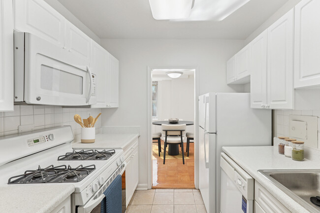 Kitchen with white cabinetry, white laminate countertops, white tile backsplash, white appliances, and hard surface flooring - The Statesman Apartments