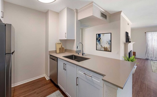 Renovated Package I kitchen with stainless steel appliances, beige quartz countertops, new white cabinetry, and hard surface flooring