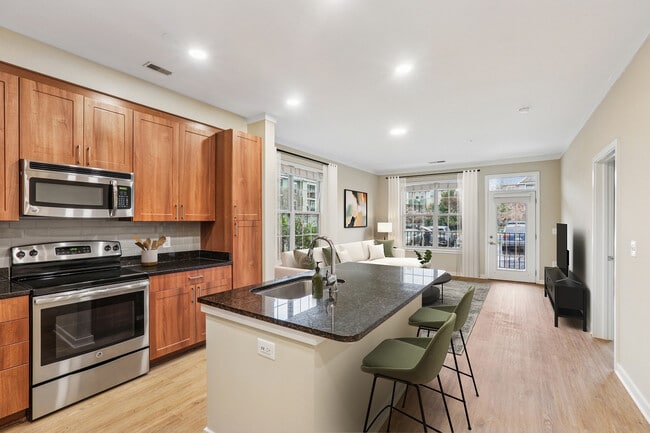 Cocina con acabados actualizados con electrodomésticos de acero inoxidable, placa para salpicaduras de azulejos grises, encimeras de granito y nuevos pisos e iluminación de superficie dura. - Avalon Falls Church